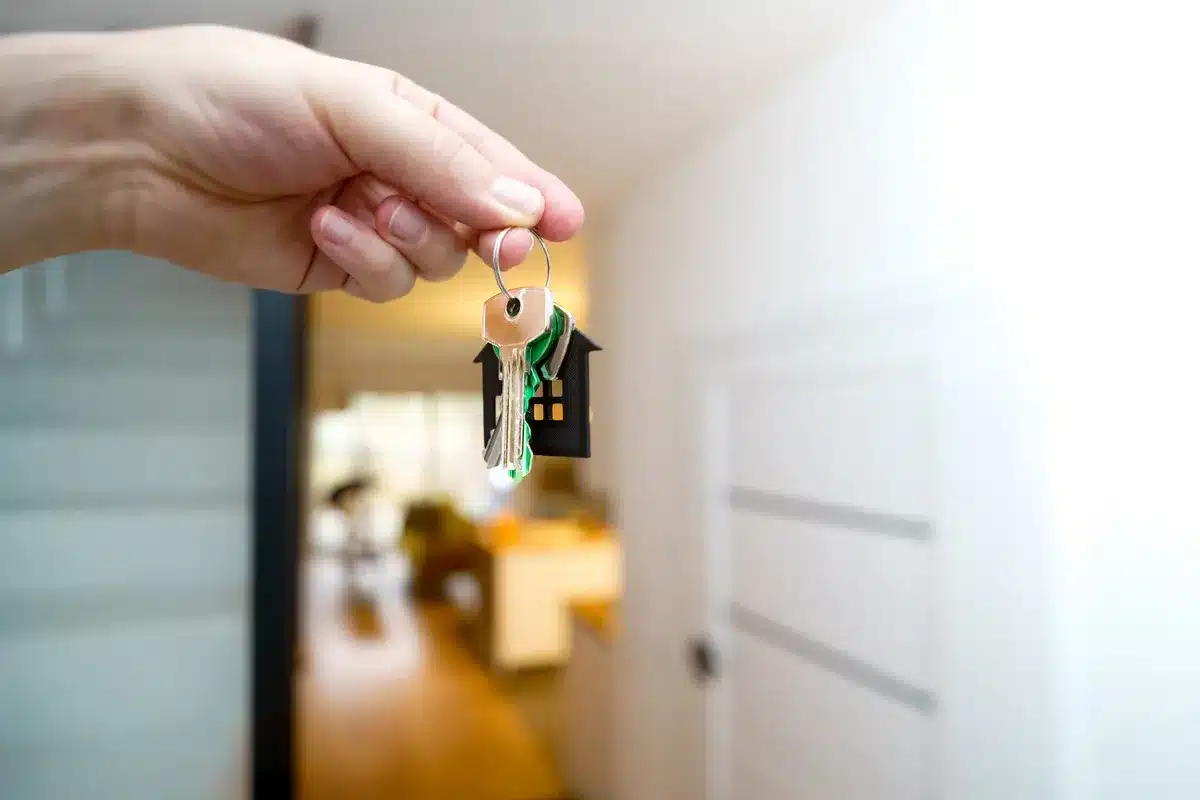 Hand hält Schlüsselbund vor offener moderner Wohnungstür mit hellem Flur im Hintergrund.