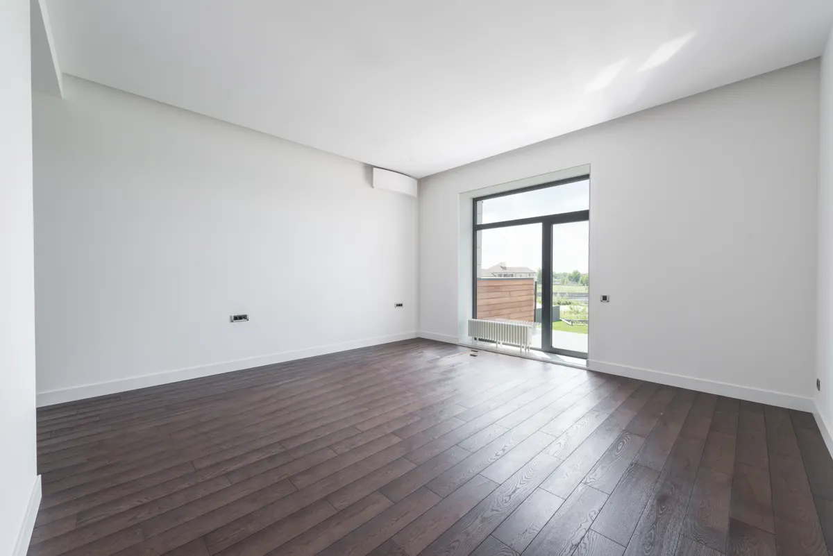 Empty bright rental flat with dark wooden parquet floor and white walls, glass door visible