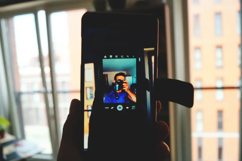 Person fotografiert moderne Balkontür mit Smartphone, Blick auf Hochhäuser im Hintergrund