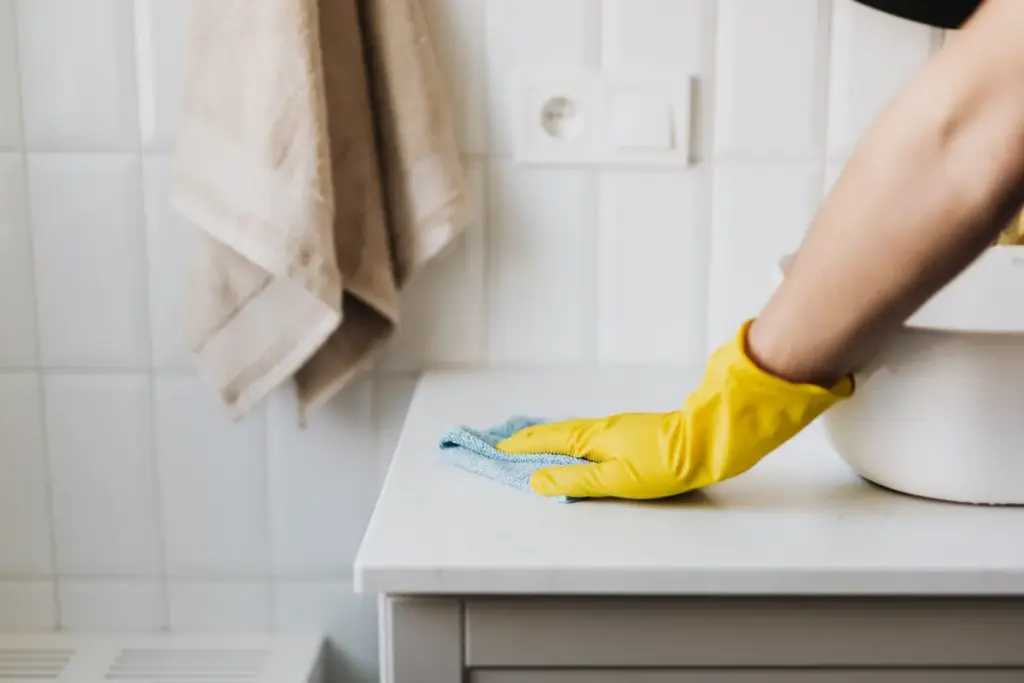 Person in yellow gloves wiping a white countertop in a bright, minimalist kitchen
