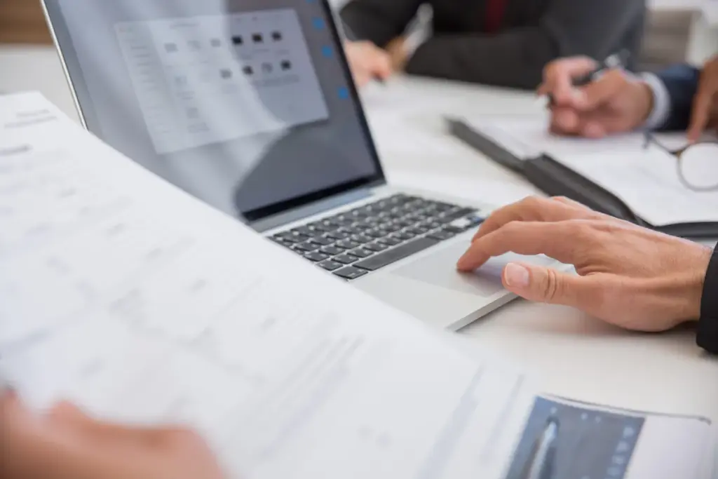 Office worker reviewing documents at desk with laptop and papers in professional setting