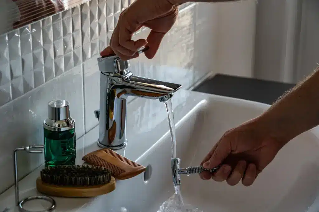 Reinigungskraft reinigt Waschbecken im sauberen Badezimmer mit grünem Reinigungsmittel.