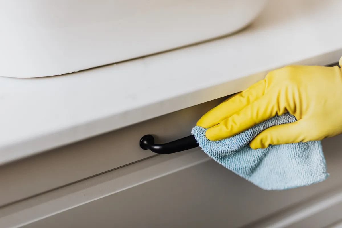 Hand in gelben Handschuhen wischt mit Mikrofasertuch über modernen Fensterrahmen.