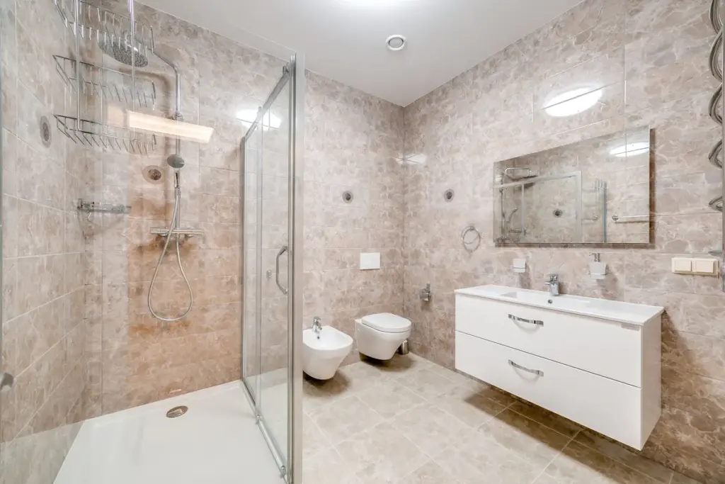 Modernes Badezimmer mit Duschglas, Waschbecken und Armaturen, helle Fliesenwände.